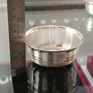 May include: A small, shiny silver bowl with a rounded shape and a decorative band around the middle. The bowl is approximately 2 inches in diameter. The image also shows a ruler with the text "MADE IN INDIA".