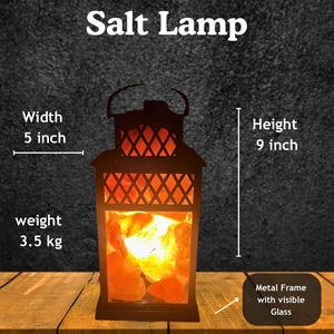 K&ouml;nnte beinhalten: Schwarze Laternen-Salzlampe mit Metallrahmen und sichtbarem Glas. Die Lampe ist 23 cm hoch und 13 cm breit und wiegt 3,5 kg. Die Lampe enth&auml;lt orangefarbene Salzkristalle und tr&auml;gt den Text "Black Lantern Salt Lamp".