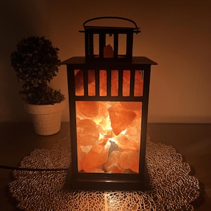 A black metal lantern filled with illuminated orange Himalayan Pink salt crystals.