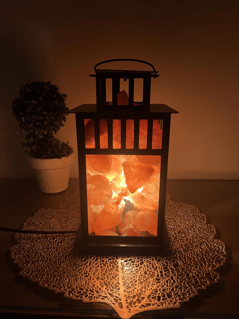 A black metal lantern filled with illuminated orange Himalayan Pink salt crystals.