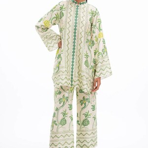 Könnte beinhalten: Cremefarbenes zweiteiliges Outfit mit grünem Blumenmuster. Das langärmlige Oberteil hat einen Stehkragen und grüne Verzierungen. Die passende Hose ist weit geschnitten. Geeignet für Freizeitkleidung.