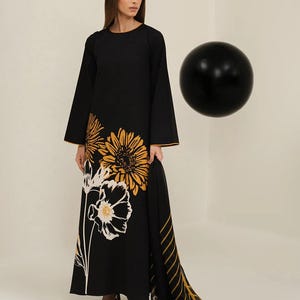 Pode incluir: Vestido longo preto com estampa floral em amarelo e branco. O vestido tem mangas compridas e um lenço a condizer com um padrão de riscas e floral. O vestido é usado com saltos pretos.