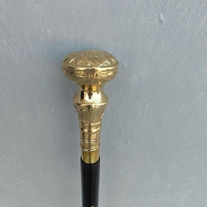 May include: A decorative walking cane with a gold-colored, ornate handle and a black shaft. The handle features detailed floral patterns and a polished finish. The cane is approximately 36 inches in length.