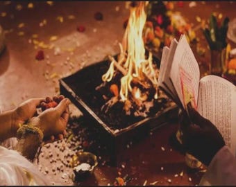 May include: A ceremonial scene featuring a burning fire in a square container. Hands hold red items and a book. The scene is set on a surface scattered with small objects and flowers, with a warm, inviting color palette.