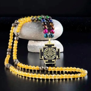 May include: A beaded necklace featuring a gold pendant with a geometric design. The necklace has yellow and gray beads, with a section of colorful beads. The pendant is black and gold.