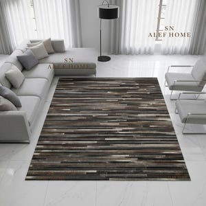 May include: A rectangular area rug featuring a horizontal striped pattern composed of various shades of brown, gray, black, and white. The rug has a textured, patchwork-style surface with linear segments. The text SN ALEF HOME is visible.