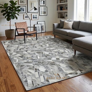 Puede incluir: Una alfombra rectangular con un patrón geométrico de retazos en tonos gris, blanco y carbón. La alfombra está compuesta por numerosas piezas angulares de varios tamaños dispuestas en un diseño de mosaico complejo sobre un suelo de madera.