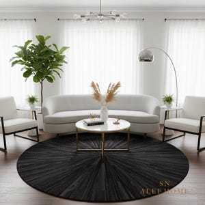 Könnte beinhalten: Ein modernes Wohnzimmer mit einem weißen Sofa, zwei weißen Sesseln und einem runden schwarzen Teppich. Ein weißer Couchtisch mit goldenen Beinen steht in der Mitte, und eine hohe grüne Pflanze befindet sich links. Eine silberne Lampe und ein Kronleuchter sorgen für Beleuchtung.