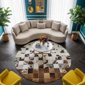 May include: A stylish living room with a curved beige sofa and cushions. A round coffee table rests on a cowhide rug. Two yellow armchairs and potted plants are placed around the sofa. The walls are teal with white trim.
