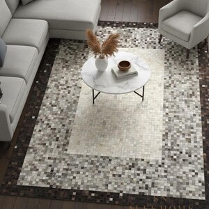 May include: A rectangular area rug with a mosaic tile pattern in shades of brown, gray, and white. The rug is bordered by a darker brown frame. A white marble coffee table and gray sofa are visible.
