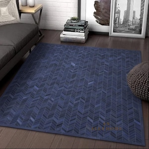 Könnte beinhalten: Ein rechteckiger blauer Teppich mit Fischgrätmuster. Der Teppich besteht aus verschiedenen Blautönen, die ein strukturiertes Aussehen erzeugen. Er liegt auf einem Holzboden und wirkt modern und stilvoll.