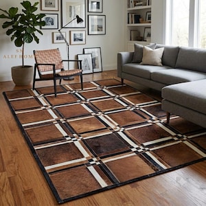 May include: A rectangular area rug featuring a patchwork design of brown, tan, and black hide squares arranged in a grid pattern. The squares are separated by thin, intersecting white and black lines that create a structured, geometric plaid effect.