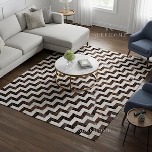 May include: A modern living room setup featuring a light gray sectional sofa, blue armchairs, and a round marble coffee table with a gold base. A brown and white chevron patterned rug covers the floor.