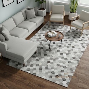 May include: An interior shot of a living room with a gray sectional sofa, two armchairs, and a round coffee table. A large area rug with a geometric pattern covers the floor. Two framed artworks hang on the wall.