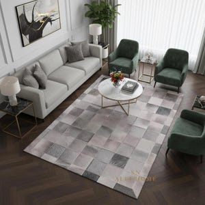 Op de afbeelding: Een woonkamer met een lichtgrijze bank, twee groene fauteuils en een patroonkleed met een geometrisch ontwerp in grijstinten en roze. Een ronde salontafel en bijzettafels maken de inrichting compleet.