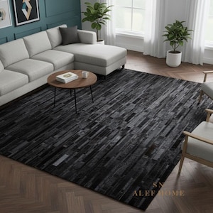 Puede incluir: Una alfombra negra rectangular grande con un patrón geométrico de diferentes tonos de gris y negro. La alfombra está en un salón con un sofá, sillas y una mesa de centro. La alfombra mide aproximadamente 244 x 305 cm.
