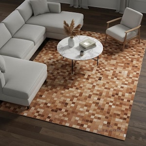 Peut inclure: Un tapis rectangulaire avec un motif géométrique de carrés beiges et bruns. Le tapis est placé sous un canapé d'angle gris clair, une table basse en marbre blanc et un fauteuil gris clair. Le tapis porte le texte "ALEE HOME".