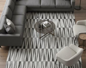 May include: A contemporary living room arrangement with a grey corner sofa, two armchairs, and a circular coffee table. A geometric rug in grey and white tones is on the floor. A black floor lamp provides illumination.