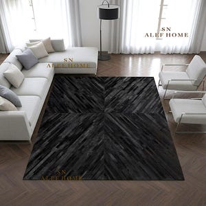 Puede incluir: Una alfombra rectangular con un patrón geométrico en gris oscuro y negro compuesto por tiras diagonales. La alfombra está situada en una sala de estar con un sofá seccional gris claro y dos sillones a juego. El texto dice SN ALEF HOME.