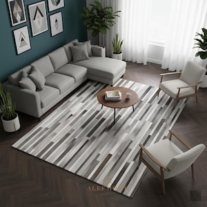 Op de afbeelding: Een moderne woonkamer met een grijze hoekbank, twee fauteuils en een ronde salontafel. Een groot vloerkleed met een streepjespatroon in grijstinten en bruin bedekt de vloer. Gekaderde kunstwerken sieren de turquoise muur.