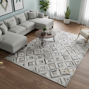 May include: A contemporary living room with a light grey sectional sofa, a round wooden coffee table, and a patterned area rug. The rug features a geometric design in grey and white. A wooden armchair and potted plants complete the interior.