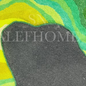 May include: A colorful rug with a vibrant, abstract design. The rug features a mix of green, yellow, and white hues, creating a layered, textured appearance. The back of the rug is visible, showing a dark gray fabric.