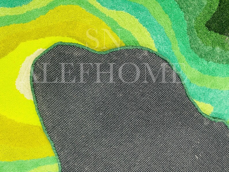 May include: A colorful rug with a vibrant, abstract design. The rug features a mix of green, yellow, and white hues, creating a layered, textured appearance. The back of the rug is visible, showing a dark gray fabric.
