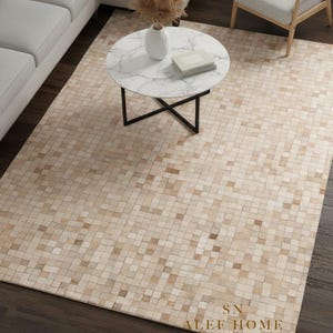 Peut inclure: Un tapis rectangulaire avec un motif en mosaïque dans des tons beiges et bruns. Le tapis est posé sur un parquet sombre, avec une table basse en marbre blanc et un canapé d'angle gris en arrière-plan. Le texte "SN ALEEF HOME" est visible sur le tapis.