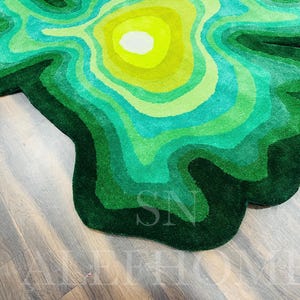May include: A green and yellow rug with a topographic design. The rug features concentric layers of varying shades of green and yellow, creating a textured, layered effect. The rug is placed on a wooden floor.