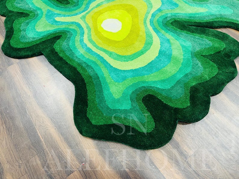 May include: A green and yellow rug with a topographic design. The rug features concentric layers of varying shades of green and yellow, creating a textured, layered effect. The rug is placed on a wooden floor.