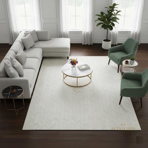 May include: A contemporary living room arrangement with a light grey sectional sofa, two green armchairs, and a marble-topped coffee table with a gold base. A patterned rug covers the floor, and a potted plant adds a touch of nature. The room is filled with natural light.