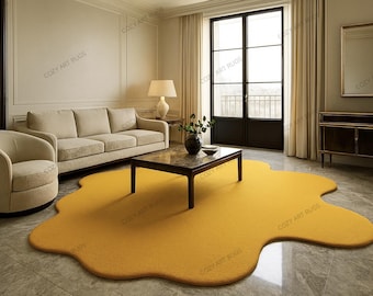 May include: A mustard yellow, organically shaped rug in a living room setting. The rug is the focal point, with a sofa, armchair, and coffee table arranged around it. The room has neutral walls and large windows.