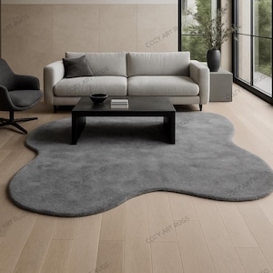 May include: A grey, organically shaped rug is the focal point in a modern living room. A light-coloured sofa, black coffee table, and a swivel chair are also visible. The rug's unique shape adds a soft contrast to the room's linear elements.