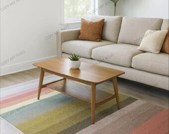 Op de afbeelding: Een woonkamer met een beige bank, houten salontafel en een veelkleurig gestreept tapijt. Het tapijt heeft horizontale strepen in roze, groen, grijs en bruin. Een kleine plant staat op de salontafel. De kamer is licht en luchtig.