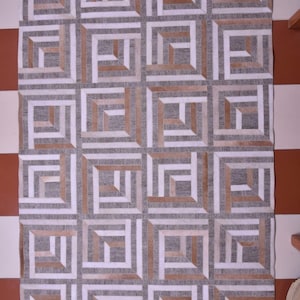 Puede incluir: Alfombra rectangular con un patrón geométrico. La alfombra presenta un diseño repetitivo de cuadrados y rectángulos en tonos grises, blancos y marrones. La alfombra está hecha de un material suave y es adecuada para una sala de estar o un dormitorio.