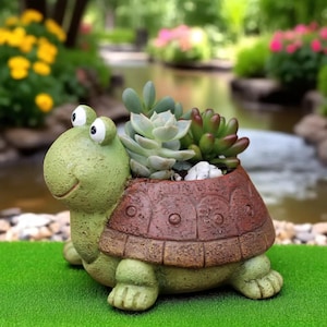 Könnte beinhalten: Ein skurriler, schildkrötenförmiger Blumentopf, bemalt in Grün- und Brauntönen, gefüllt mit Sukkulenten. Die Schildkröte hat ein lächelndes Gesicht und große Augen. Der Topf steht auf einer grünen Oberfläche, mit einem verschwommenen Gartenhintergrund.