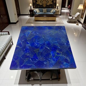 Könnte beinhalten: Ein großer, quadratischer Couchtisch mit einer leuchtend blauen Lapislazuli-Oberfläche. Die Steinoberfläche ist ein Mosaik aus tiefen Blautönen und goldenen Akzenten. Der Tisch steht auf einem dunklen, verzierten Gestell und ist ein luxuriöses Möbelstück.