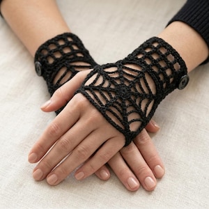 May include: A pair of black fingerless gloves crafted from crochet yarn in a spiderweb pattern. Each glove features a circular web design on the back of the hand and is secured at the wrist with a small, round, black button closure.
