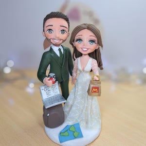 May include: A wedding cake topper depicting a bride and groom. The groom holds a laptop and a can of Coca-Cola, while the bride carries a McDonald's bag. A map and suitcase are also included. The groom is wearing a green suit, and the bride is wearing a white wedding dress.