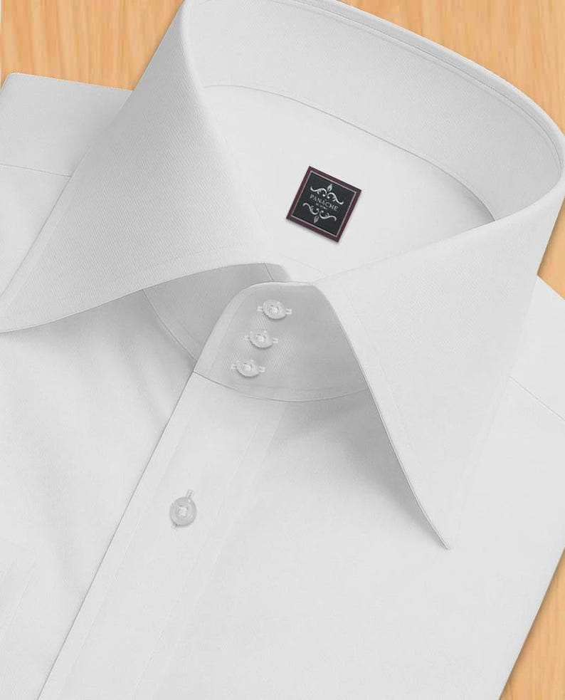 May include: A close-up of a white dress shirt with a high collar and three small buttons near the collar. The shirt features a small label with the word "PANACHE". The shirt is made of a smooth, likely cotton, fabric.