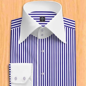 以下が含まれることがあります： 青と白のストライプのドレスシャツ。白い襟と袖口があり、小さなボタンが付いています。襟の近くには小さなエンブレムが見えます。木製の表面に置かれています。