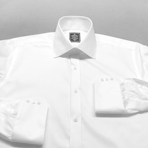 May include: A pristine white dress shirt with a traditional collar and buttoned cuffs. The shirt has a button-down front and a small label near the collar. The sleeves are folded up, displaying the cuff details.