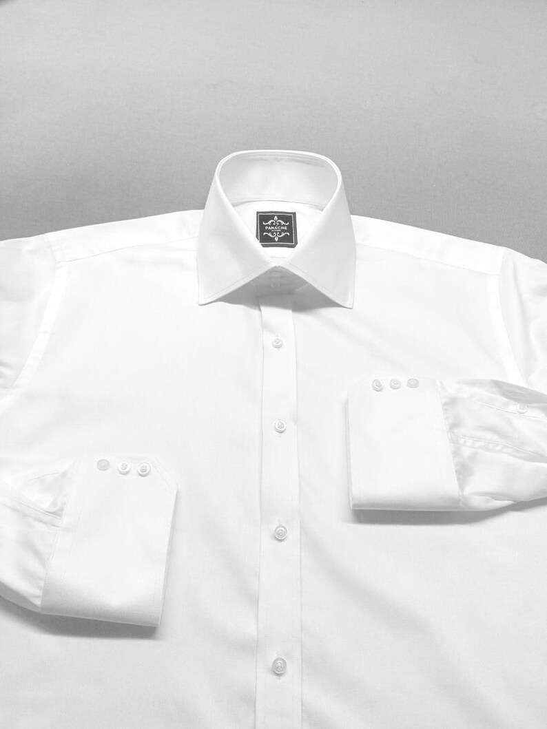 May include: A pristine white dress shirt with a traditional collar and buttoned cuffs. The shirt has a button-down front and a small label near the collar. The sleeves are folded up, displaying the cuff details.