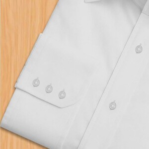 May include: A close-up view of a white dress shirt. The shirt has a classic collar, a button-down front, and a buttoned cuff with three buttons. The fabric looks smooth and crease-free, indicating a high-quality material.