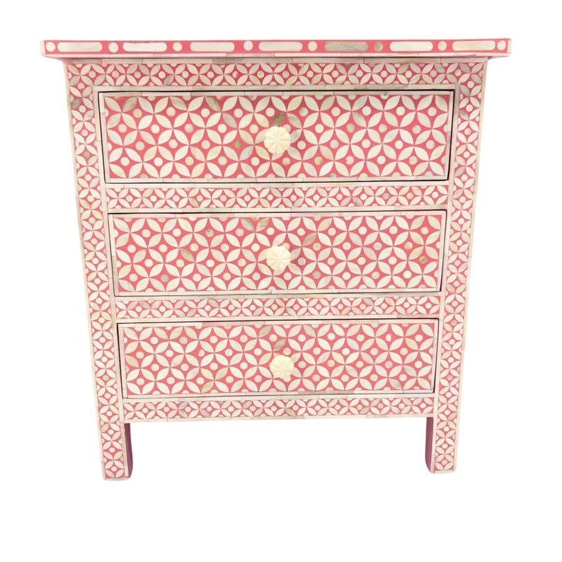 May include: A three-drawer chest of drawers with a geometric pattern in red and white. The chest has a rectangular shape with a decorative border and cream-colored knobs. The measurements are approximately 30 inches tall, 24 inches wide, and 16 inches deep.