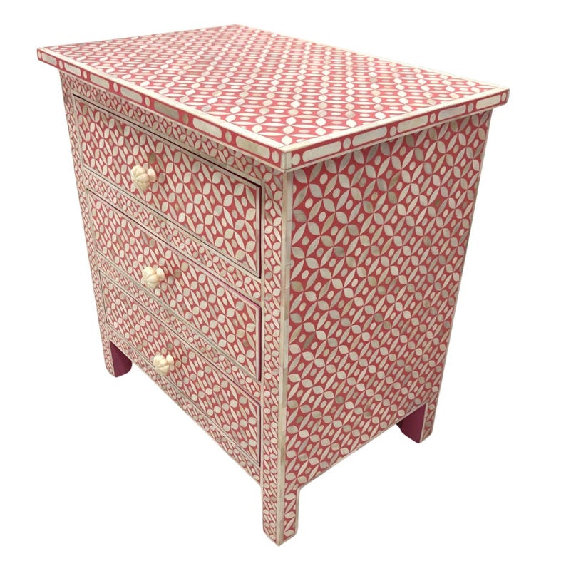 May include: A red and white patterned nightstand with three drawers. The nightstand features a geometric design with white accents and floral-shaped drawer pulls. The piece is approximately 24 inches tall, 18 inches wide, and 14 inches deep.