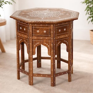 Puede incluir: Mesa auxiliar octogonal de madera con incrustaciones florales. Los cajones y la tapa están adornados con patrones. Las patas son decorativas. La madera tiene un tono marrón cálido. Medidas: aprox. 76 cm de alto y 60 cm de ancho.