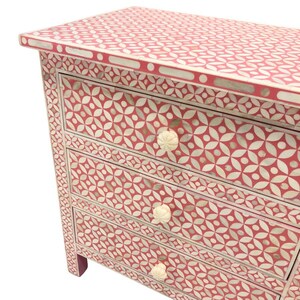 May include: A four-drawer chest of drawers with a red and white floral pattern. The chest has a rectangular shape with a flat top and decorative white knobs. The pattern is repeated on the top, sides, and drawer fronts.