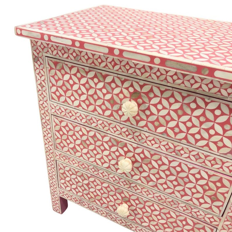 May include: A four-drawer chest of drawers with a red and white floral pattern. The chest has a rectangular shape with a flat top and decorative white knobs. The pattern is repeated on the top, sides, and drawer fronts.