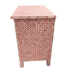 May include: A red and white patterned cabinet with a geometric design. The cabinet has a rectangular shape with four short legs. The pattern is made up of circles and petal-like shapes. The cabinet is a decorative piece of furniture.